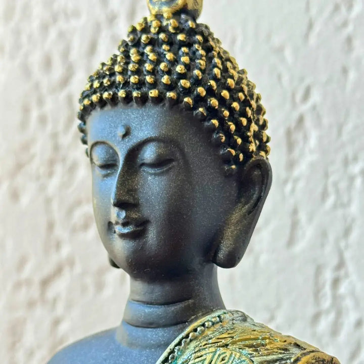 Close-up da cabeça da estátua de Buda em resina, mostrando o acabamento dourado nos cabelos e expressão serena do rosto.