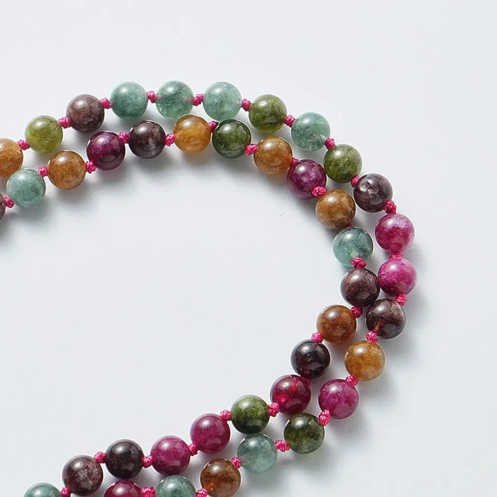 Detalhe das contas de turmalina natural do japamala Samadhi – pedras de 8mm com cores vibrantes e fio rosa, fundo branco claro