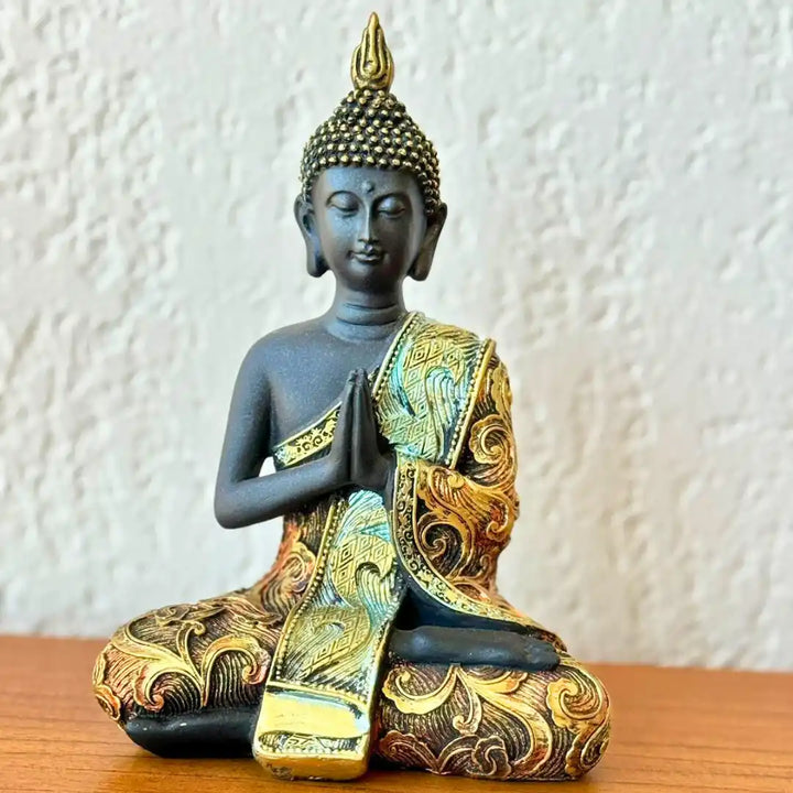Estátua de Buda em resina, de frente, com acabamento dourado detalhado no manto e postura de mãos em Mudra de Gratidão, representando serenidade e paz.