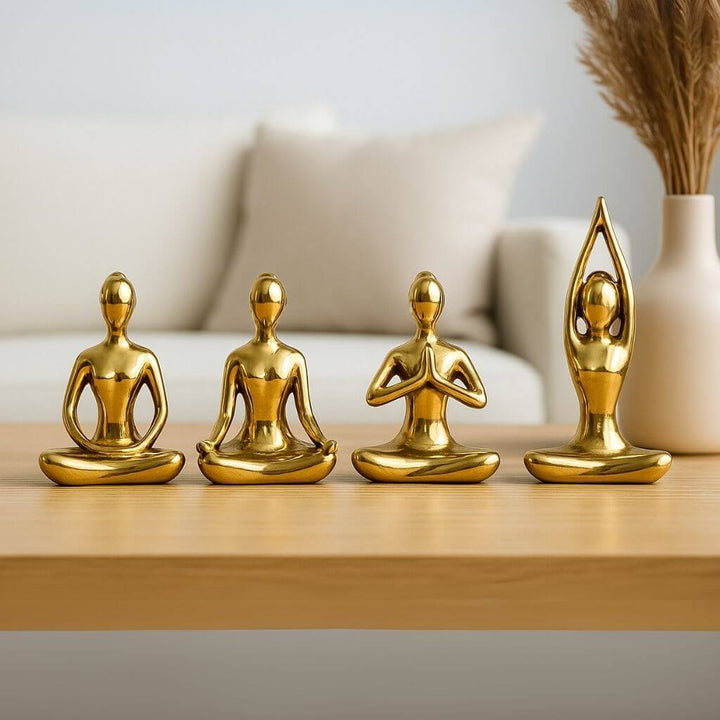 Kit com estatuetas douradas de yoga em cerâmica sobre mesa de madeira, decorando sala com estilo zen e espiritualidade.