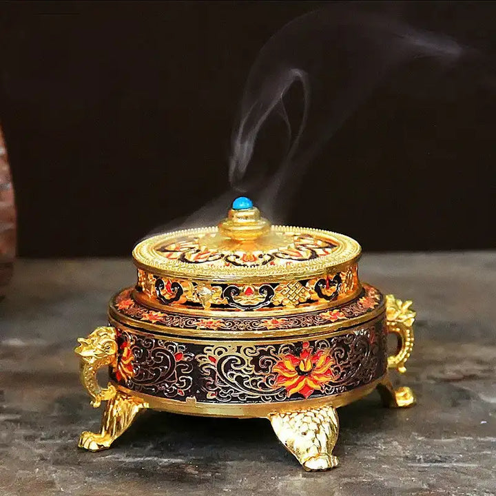 Incensário dourado com detalhes em vermelho e azul, liberando fumaça de incenso.