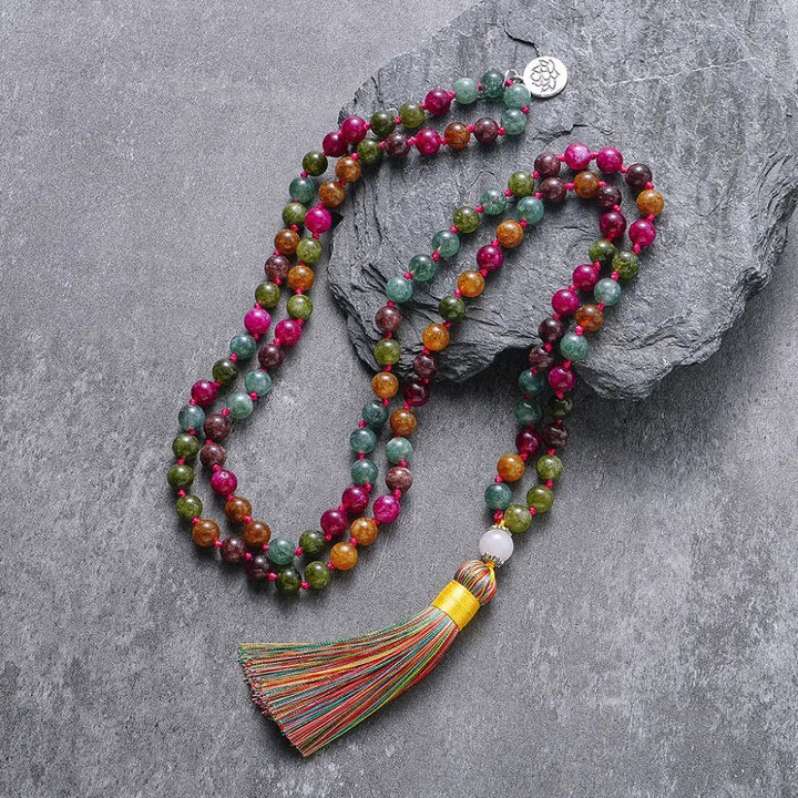 Colar japamala Samadhi com turmalinas coloridas e tassel amarelo, posicionado sobre pedra escura – acessório espiritual para práticas de meditação